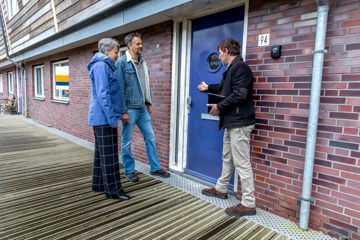 Drie mensen bij een voordeur van een appartement