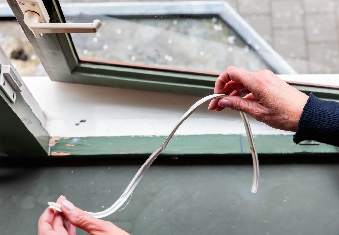 Vrouw haalt oude tochtband weg, zodat ze het kan vervangen voor nieuwe.