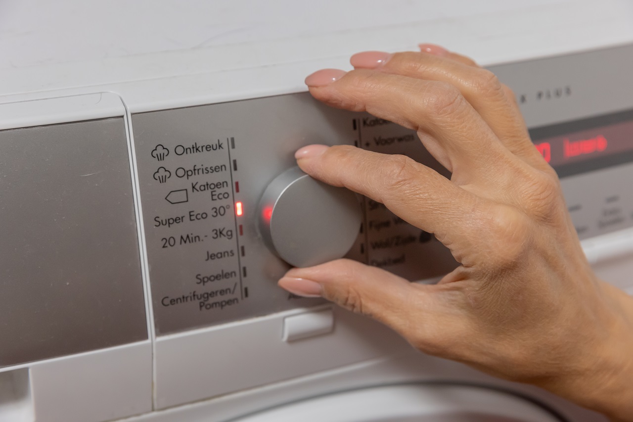 Iemand zet de wasmachine op de ecostand om energie te besparen.