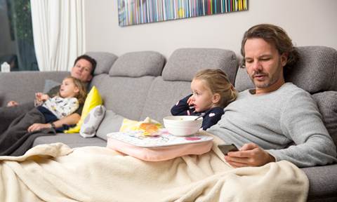 Man met kinderen onder deken op bank. Met een deken verwarm je energiezuinig.