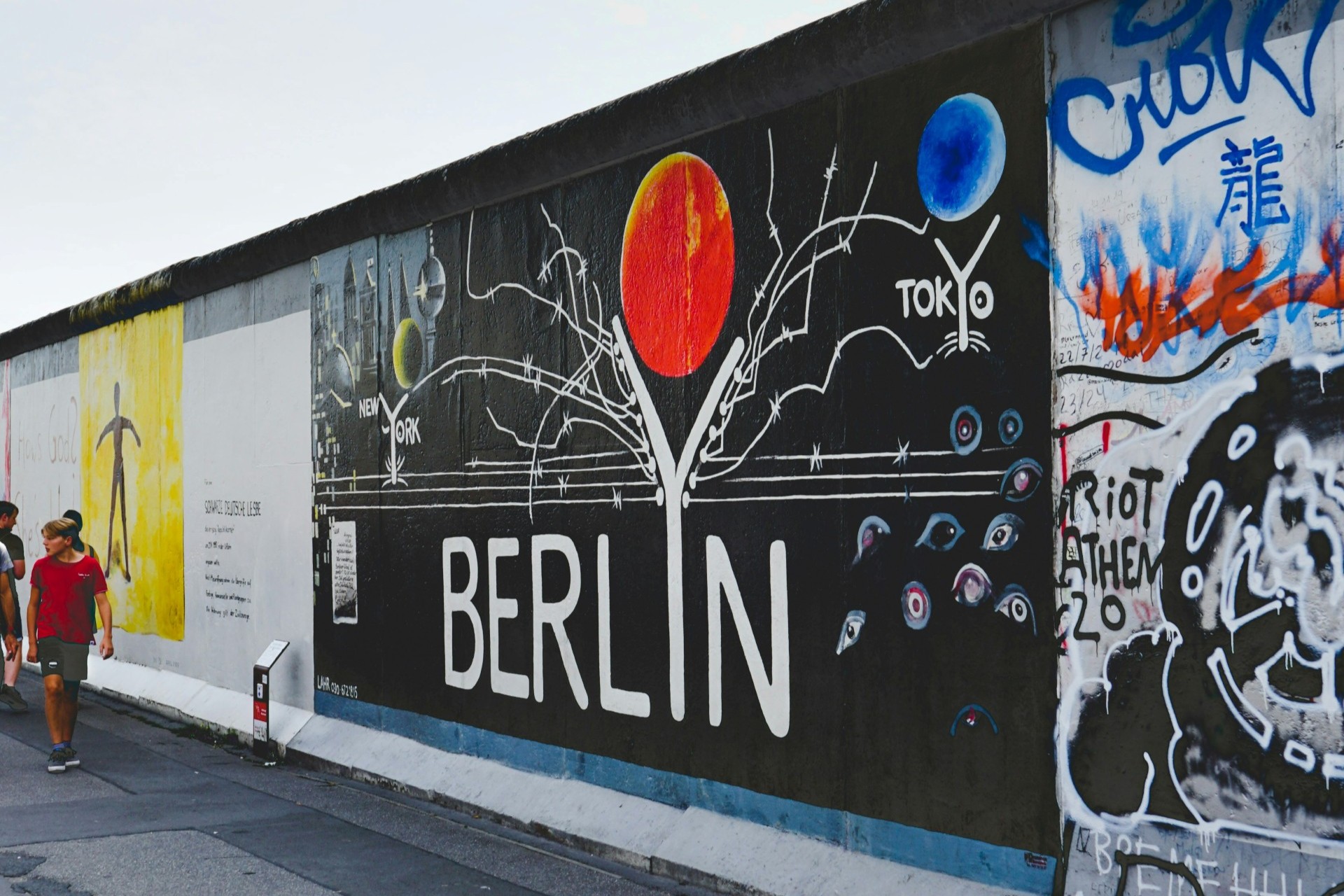 Foto van een muurschildering op een stuk muur in Berlijn. De muurschildering is zwart, laat een rode bol zien en heeft in witte letter de tekst Berlijn.